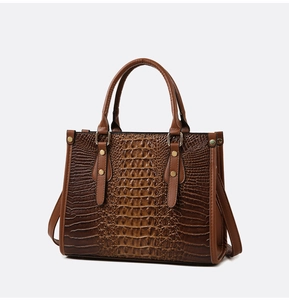 Detail of crocodile embossed texture on brown tote bag with gold hardware and rivets