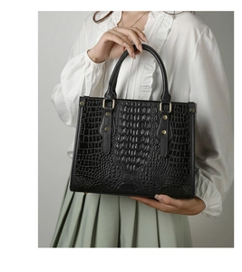 Detail of black crocodile embossed tote bag featuring gold studs and dual handles
