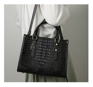 Detail of black crocodile texture tote bag with gold rivets and shoulder strap