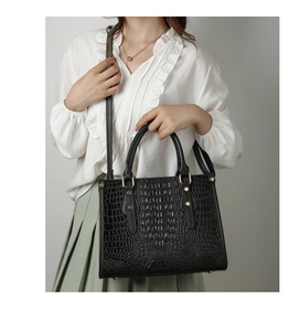 Detail of black crocodile texture tote bag with gold hardware shown on a model