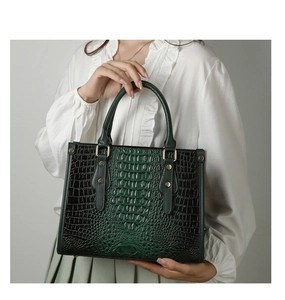 Detail view of dark green handbag with crocodile pattern texture and gold metal hardware