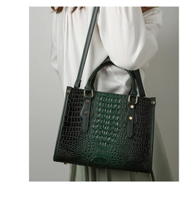 Detail of dark green crocodile embossed tote bag with gold studs and top handles