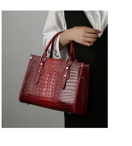 Detail of dark red faux crocodile tote bag with gold rivets and handle texture