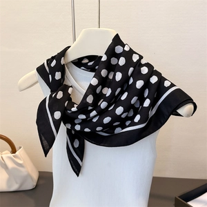 Elegant black silk scarf with white polka dots draped over a minimalist white vest