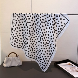 Silk-like square scarf with geometric black polka dots draped over a cream handbag
