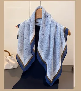 Detail of blue and white floral cotton scarf hanging on a wooden hanger with a beige handbag