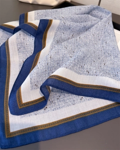 Macro detail of herringbone linen texture scarf with blue border and golden wave pattern