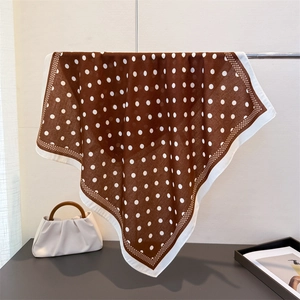 Detail of coffee brown polka dot silk scarf hanging on a metal rod for luxury display
