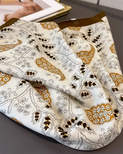 Close-up of beige silk scarf with brown paisley pattern and twill texture on a tray