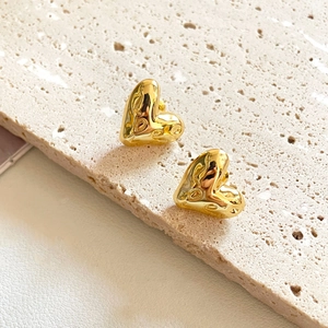 Macro detail of gold-plated heart earrings with textured finish on beige stone surface