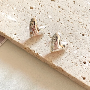 Macro view of 3D puffy silver heart stud earrings with engraved Love pattern detail