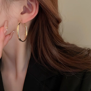 Close-up of a large polished 18K gold plated hoop earring worn by a model