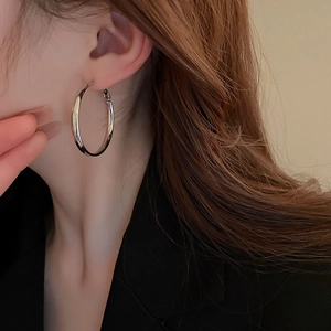 Close-up of model wearing polished silver-plated oversized hoop earrings in a minimalist style
