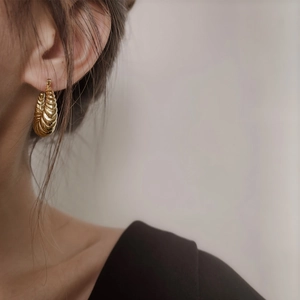 Gros plan d'une boucle d'oreille croissant dorée avec une texture torsadée mate