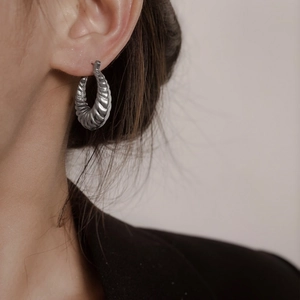 Gros plan de boucles d'oreilles créoles argentées avec motif torsadé texturé