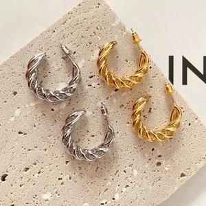 Macro detail of twisted hoop earrings in gold and silver finish on stone tray