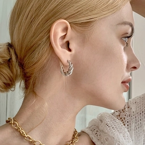 Close-up of silver-plated twisted rope hoop earrings worn by a model in a high-fashion style