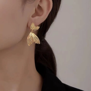 Detailed close-up of a gold fishtail earring with textured fan-shaped layers on a model