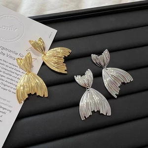 Detail shot of gold and silver fishtail earrings on a professional black display tray
