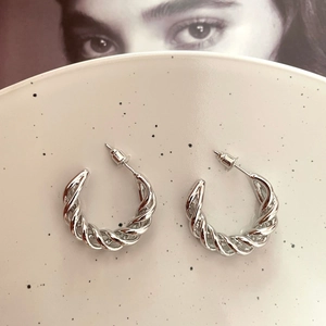 Detailed view of silver twisted hoop earrings on a ceramic tray with magazine backdrop