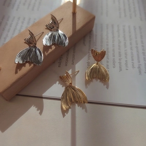 Detailed close-up of overlapping fishtail earrings in gold and silver metallic finishes