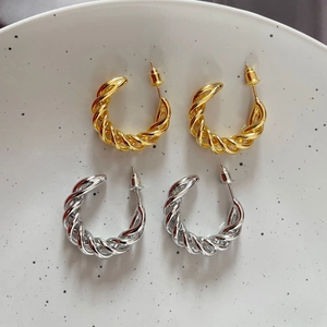 Detail of gold and silver twisted hoop earrings with textured finish on ceramic tray