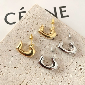 Polished gold and silver C-shaped metallic stud earrings on a textured stone base
