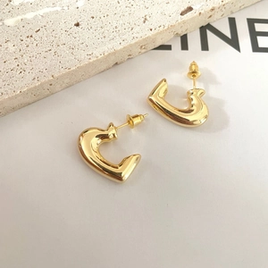 Detailed view of polished gold irregular heart earrings on a white card with stone