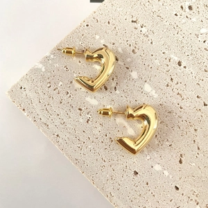Polished gold heart-shaped earrings displayed on a textured stone aesthetic platform