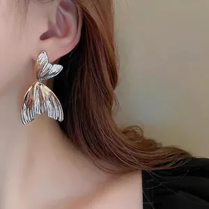 Elegant silver fishtail dangle earrings with textured metallic finish on model