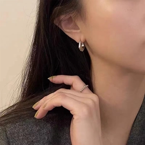 Détail macro de boucles d'oreilles fer à cheval argentées et bague perlée sur modèle