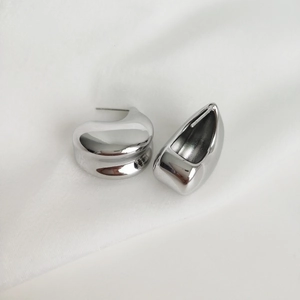 Macro view of polished silver C-shape earrings on white silky fabric background