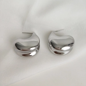 Macro shot of silver drop earrings with polished finish on white satin background