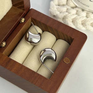 Polished silver crescent hoops shown in a luxury wooden jewelry box display