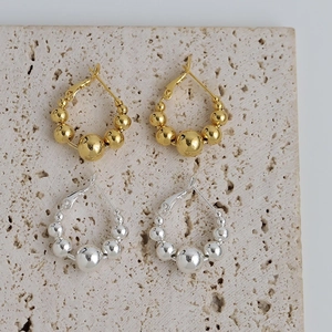 Boucles d'oreilles créoles perlées dorées et argentées sur un support en pierre