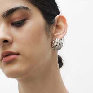 Minimalist silver shell-shaped earrings with metallic texture worn by a model