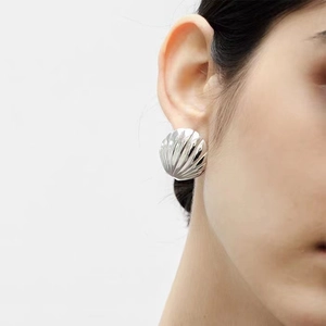 Silver shell earrings with textured metallic finish on model in close-up shot
