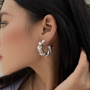 Fashionable oversized silver spiral twisted C-shape hoop earrings worn by a female model