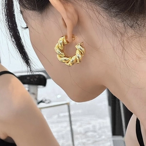 Close-up of a gold twisted hoop earring with a polished spiral texture on a female model