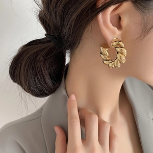 Close-up of golden chunky twisted C-shaped hoop earrings on a model showing metallic texture