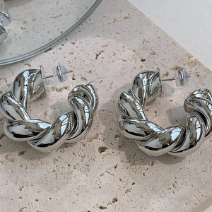 Macro shot of silver twisted hoop earrings with rope texture on a stone surface