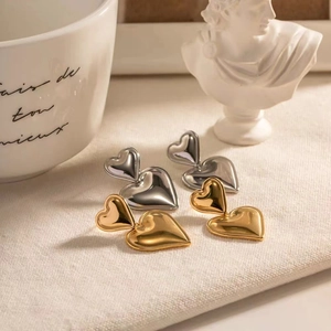 Exquisite 18K vergoldete Doppelherz-Ohrringe präsentiert neben einer klassischen Skulptur