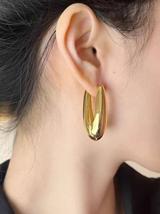 Close-up of model wearing polished gold teardrop earrings with a sleek metallic finish