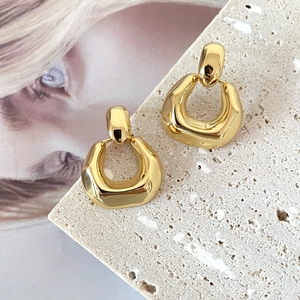 Polished 18K gold plated geometric U-shaped hoop earrings on a stone display base