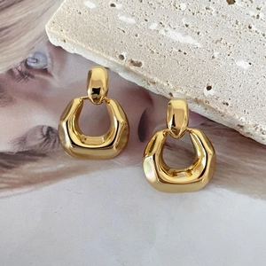 Polished 18K gold plated geometric earrings displayed on textured stone and fashion magazine