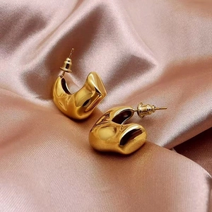 Polished gold irregular crescent C-shape earrings on elegant champagne silk fabric