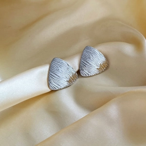 Silver triangle stud earrings with brushed metal texture on champagne silk background