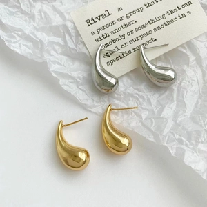 Dettaglio macro di orecchini a goccia lucidi color oro e argento su espositore bianco