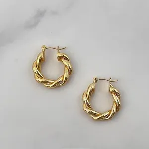Gros plan détaillé de boucles d'oreilles créoles torsadées dorées sur marbre