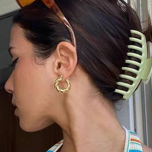 Détail de créoles torsadées dorées et d'une pince à cheveux mate vert clair